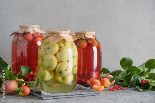 Fototapeta Naklejka Na Ścianę i Meble -  Three homemade canned fruits apple and cherry compote in large glass jars on gray table.