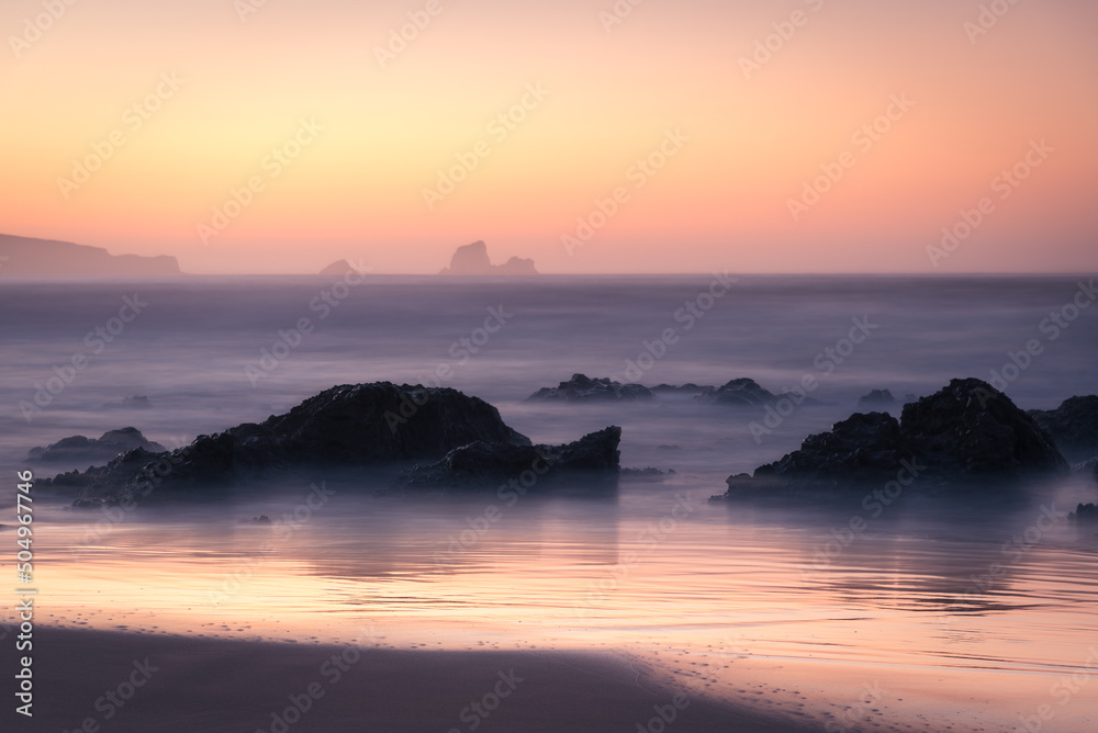 Beautiful dreamlike sunset on the beach with waves reaching the shore and rocks on the sand, Dunas de Liencres Natural Park and Costa Quebrada, Cantabria, Spain