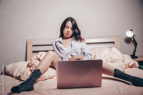 a young Asian webcam model girl is sitting in front of a laptop with her legs spread. she communicates and shows her charms. low depth of focus,artistic photo processing