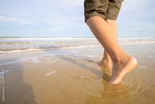 Fotografie Closeup legs of a young girl stepping on the water and sand barefoot, and walking closer to the sea