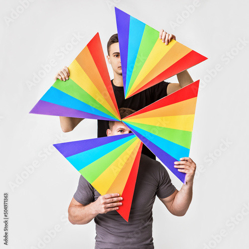 two young men hold triangles with the rainbow pattern in front of their faces, concept of LGBTQ pride, LGBTQ rights campaign