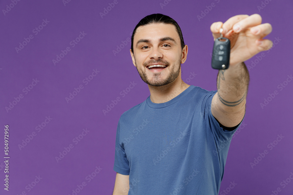 Young smiling cheerful fun cool man 20s wearing basic blue t-shirt hold giving close up car keys fob keyless system isolated on plain purple color background studio portrait. People lifestyle concept. Young smiling cheerful fun cool man 20s wearing basic blue t-shirt hold giving close up car keys fob keyless system isolated on plain purple color background studio portrait. People lifestyle concept.