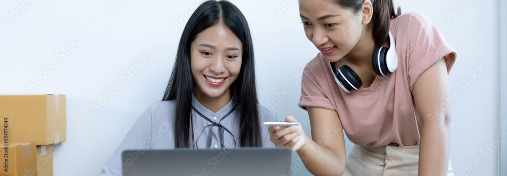 Two young Asian women chat with bright smiles to customers who shop online via laptop and confirm the order to close the deal, Selling products online or doing freelance work at home concept. Two young Asian women chat with bright smiles to customers who shop online via laptop and confirm the order to close the deal, Selling products online or doing freelance work at home concept.