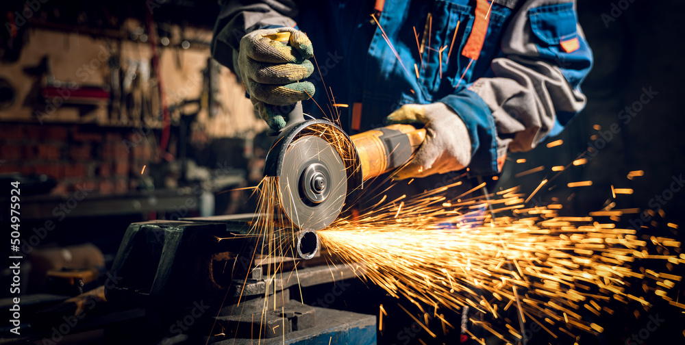 Locksmith in special clothes and goggles works in production. Metal processing with angle grinder. Sparks in metalworking - obrazy, fototapety, plakaty 
