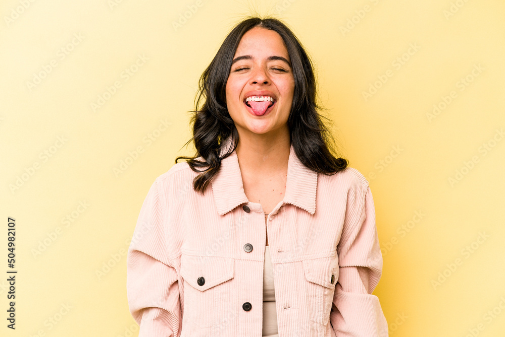 Young hispanic woman isolated on yellow background funny and friendly sticking out tongue. Young hispanic woman isolated on yellow background funny and friendly sticking out tongue.