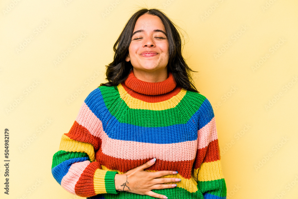 Young hispanic woman isolated on yellow background touches tummy, smiles gently, eating and satisfaction concept. Young hispanic woman isolated on yellow background touches tummy, smiles gently, eating and satisfaction concept.