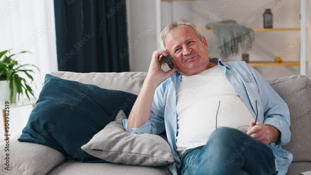 Cheerful old man talking by phone while sitting on the sofa at home Cheerful old man talking by phone while sitting on the sofa at home