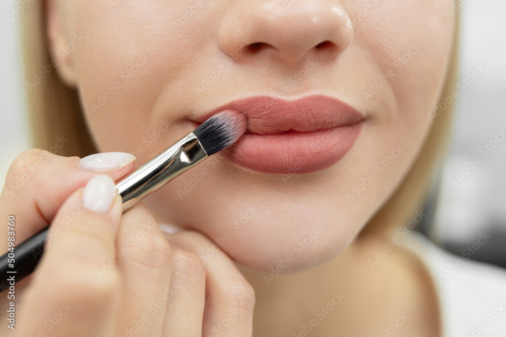 Make-up artist cosmetologist paints her lips before a permanent makeup procedure.