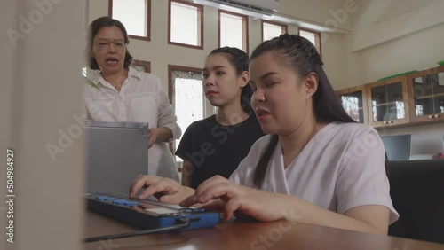 Wide angle shot of Asian women co-workers in workplace including person with blindness disability using computer with refreshable braille display assistive device. Disability inclusion at work concept