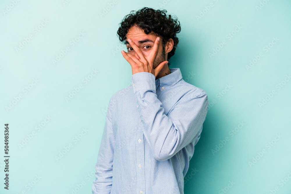 Young caucasian man isolated on white background blink at the camera through fingers, embarrassed covering face.