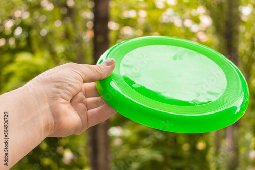 A hand with a disc for playing frisbee on the background of the park. The concept of mobile games.