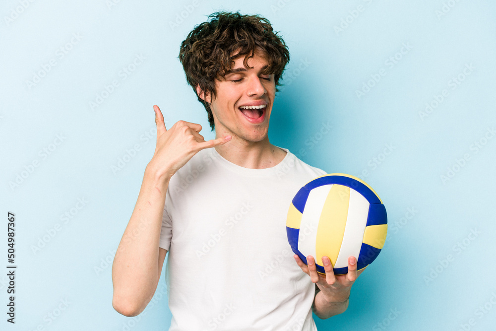 Young caucasian man playing volleyball isolated on blue background showing a mobile phone call gesture with fingers.