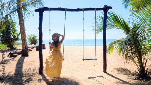 Woman with hat enjoying freedom on swing in Phuket  Thailand. Life  adventure and travel concept. Happy young woman in long dress on swing enjoy summer vacation in tropical resort with sea view