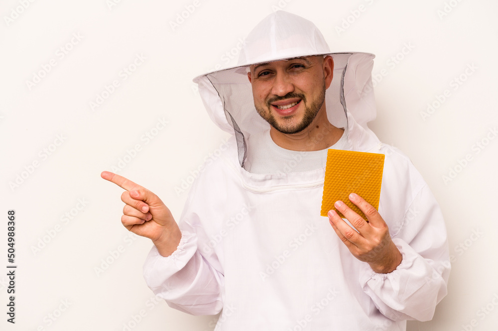 Hispanic beekeeper man holding honey isolated on white background smiling and pointing aside, showing something at blank space. Hispanic beekeeper man holding honey isolated on white background smiling and pointing aside, showing something at blank space.