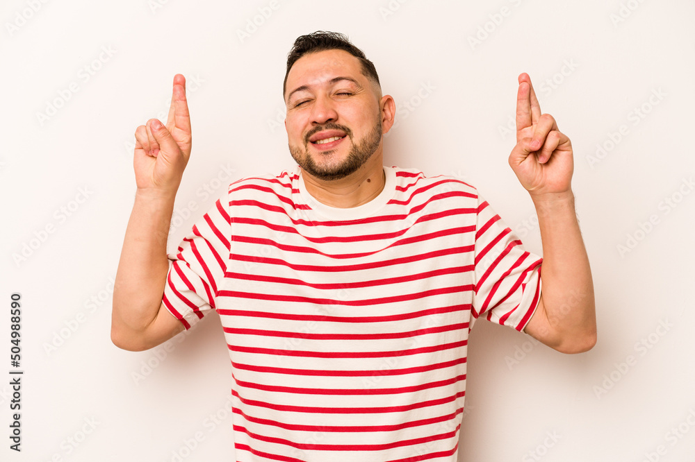 Young hispanic man isolated on white background crossing fingers for having luck Young hispanic man isolated on white background crossing fingers for having luck