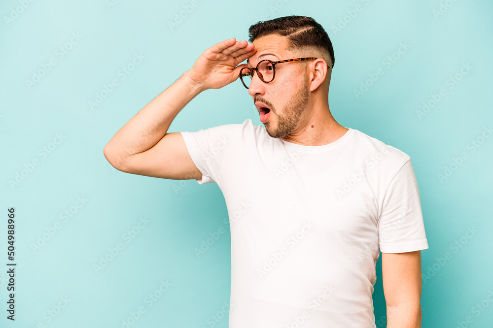 Young hispanic man isolated on blue background looking far away keeping hand on forehead. Young hispanic man isolated on blue background looking far away keeping hand on forehead.