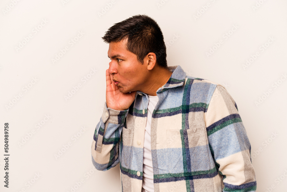 Young hispanic man isolated on white background is saying a secret hot braking news and looking aside