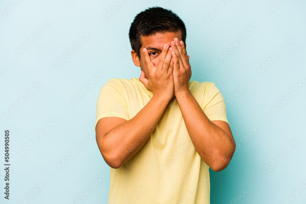 Young hispanic man isolated on blue background blink through fingers frightened and nervous. Young hispanic man isolated on blue background blink through fingers frightened and nervous.