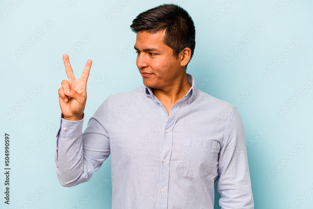 Young hispanic man isolated on blue background joyful and carefree showing a peace symbol with fingers.