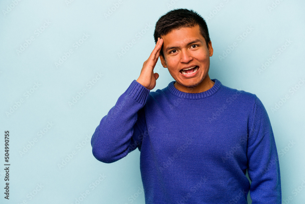 Young hispanic man isolated on blue background shouts loud, keeps eyes opened and hands tense. Young hispanic man isolated on blue background shouts loud, keeps eyes opened and hands tense.