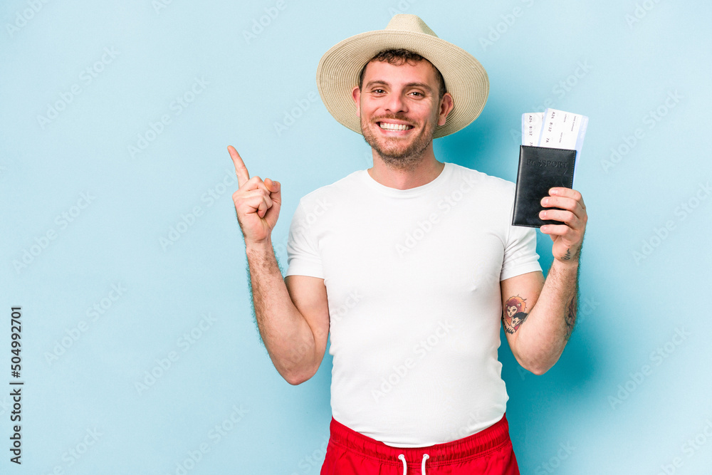 Young caucasian traveler man holding passport isolated on blue background smiling and pointing aside, showing something at blank space. Young caucasian traveler man holding passport isolated on blue background smiling and pointing aside, showing something at blank space.