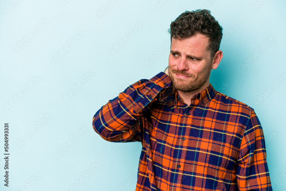 Young caucasian man isolated on blue background touching back of head, thinking and making a choice. Young caucasian man isolated on blue background touching back of head, thinking and making a choice.