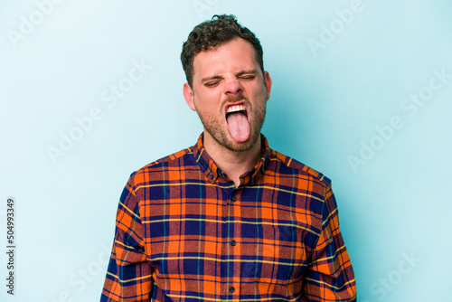 Canvas Young caucasian man isolated on blue background funny and friendly sticking out tongue