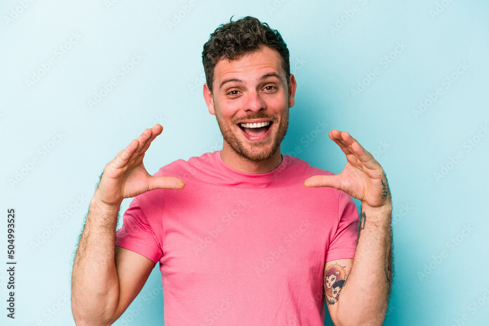 Young caucasian man isolated on blue background holding something with palms, offering to camera. Young caucasian man isolated on blue background holding something with palms, offering to camera.