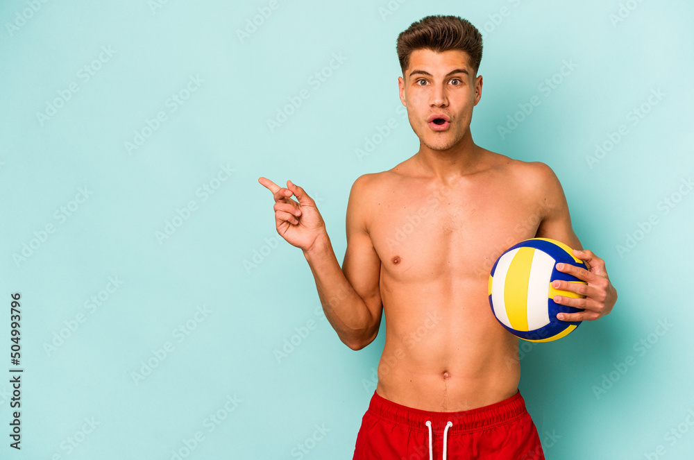 Young caucasian man playing volley isolated on blue background pointing to the side