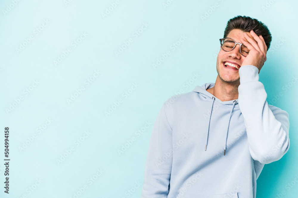 Young caucasian man isolated on blue background laughing happy, carefree, natural emotion.