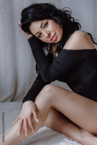 Beautiful girl in a revealing black clothes posing on the bed on a light background. Female body and style concept.