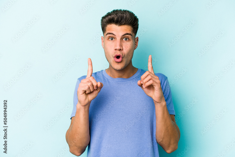 Young caucasian man isolated on blue background pointing upside with opened mouth. Young caucasian man isolated on blue background pointing upside with opened mouth.