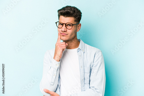 Young caucasian man isolated on blue background unhappy looking in camera with sarcastic expression. © Asier