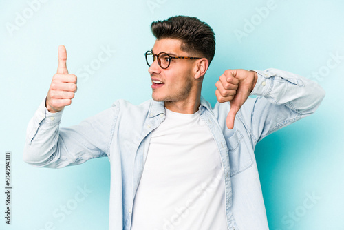 Young caucasian man isolated on blue background showing thumbs up and thumbs down, difficult choose concept