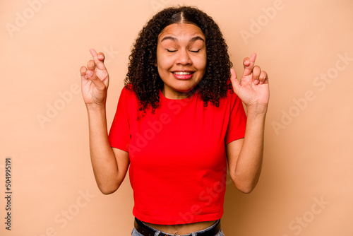 Young African American woman isolated on beige background crossing fingers for having luck