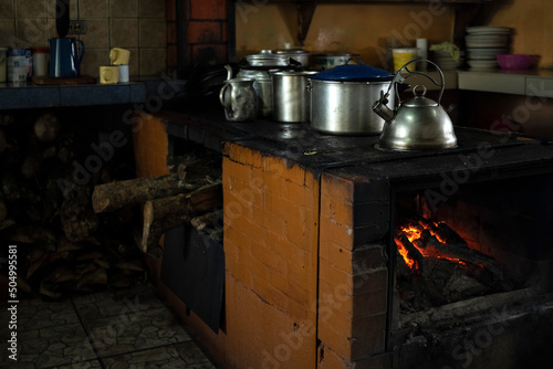 Traditional kitchen with wood stove burning and metal pots and pans.