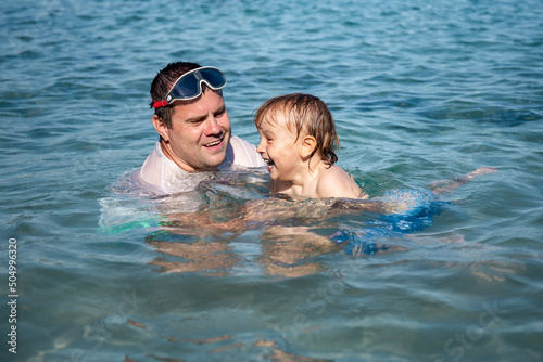 Father and little son having fun swimming and playing together in sea water at summer holidays. Family bonding, togetherness. Seaside vacation.