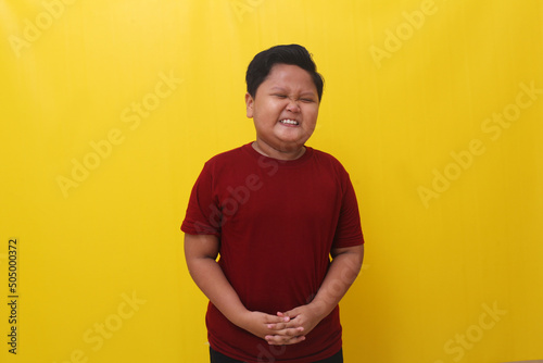 Asian boy standing up wincing in pain. Isolated on yellow background photo