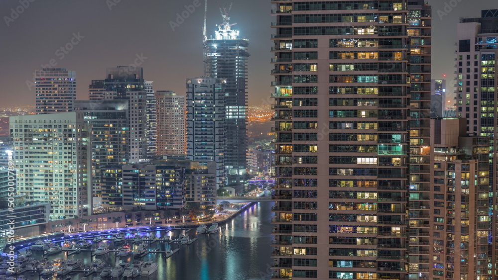 Aerial view to Dubai marina skyscrapers around canal with floating boats night timelapse