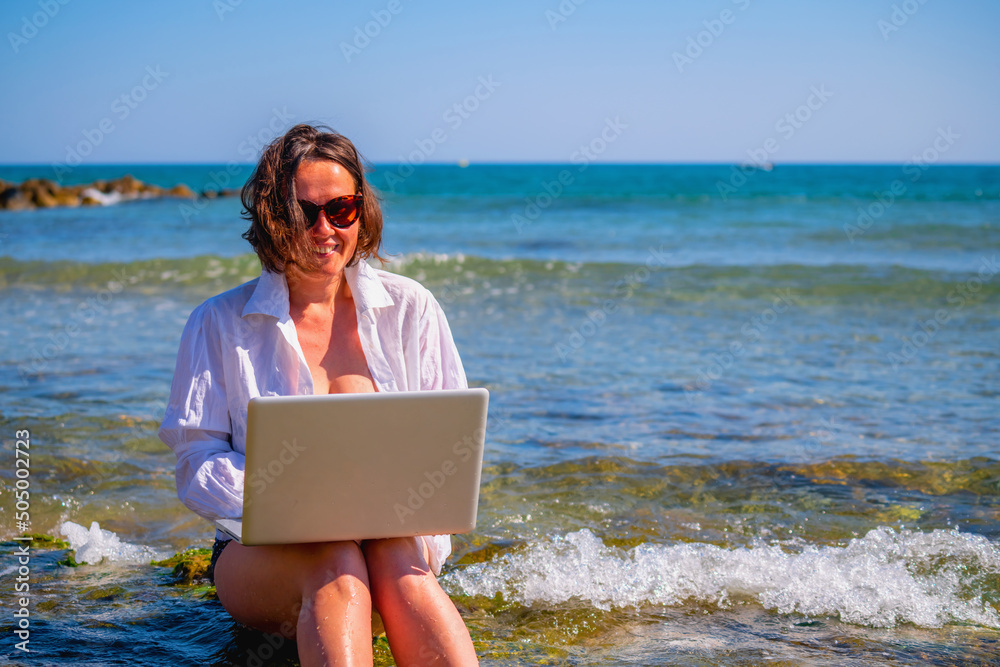 Happy business woman working remotely and using laptop computer on a beach by the sea. Copy space.