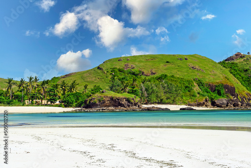 Beautiful paradise landscape, empty lonely white sand beach, turquoise water lagoon, lush green rock stone hill, blue summer sky, fluffy clouds - Kuta , Lombok, Indonesia