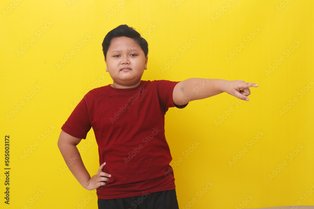 Smiling asian boy standing while pointing something beside him. Isolated on yellow background Smiling asian boy standing while pointing something beside him. Isolated on yellow background
