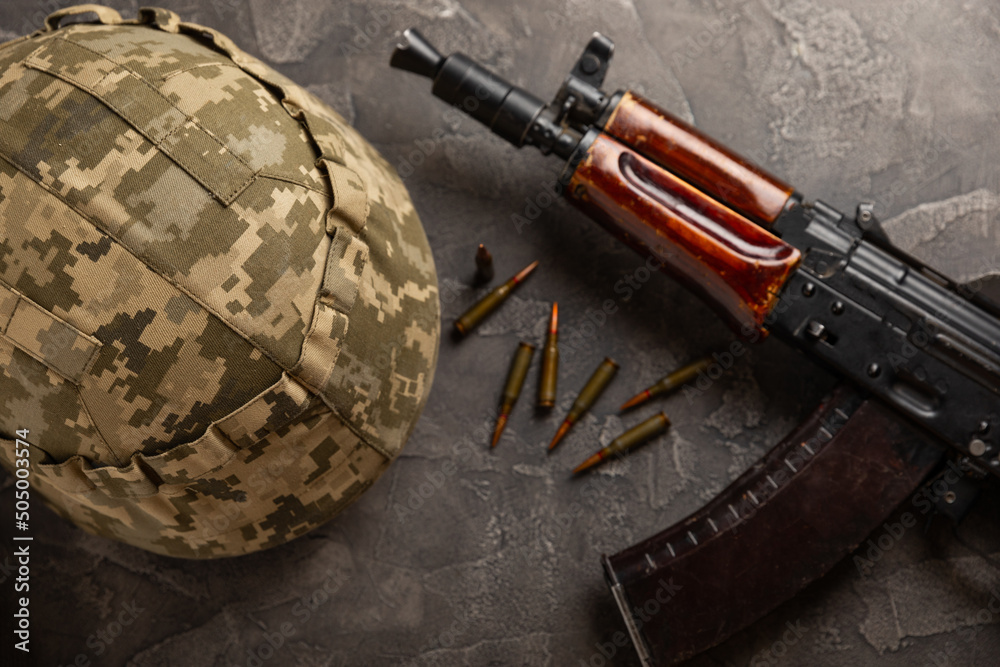 Fototapeta premium Bullets and ammo magazine with Kalashnikov assault rifle and hard hat on black textured marble. Composition with place for text. Cartridges for a rifle and a carbine on a wooden background. Military c