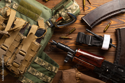 Valokuva Army body armor, helmet and ammunition, Kalashnikov assault rifle with matrons and first aid tourniquet composition on brown wood