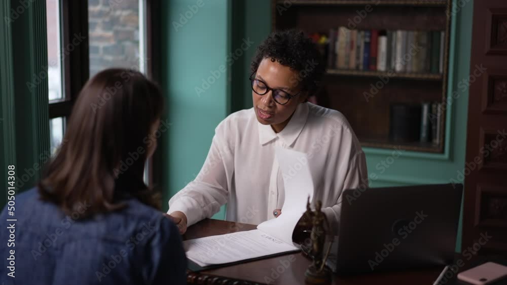 Young female lawyer talking to client and showing document at table in modern office spbas. 4k Two multiethnic women talk with smiles and look at paper lawsuit, do legal work and sit at desk with Young female lawyer talking to client and showing document at table in modern office spbas. 4k Two multiethnic women talk with smiles and look at paper lawsuit, do legal work and sit at desk with