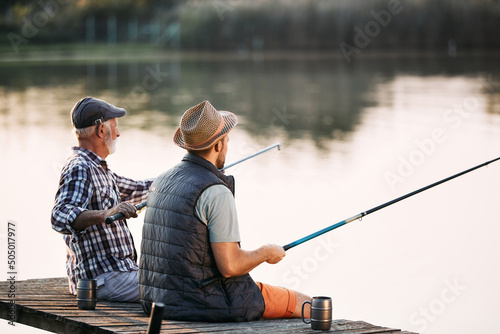 Rear view of senior man and his son fishing from pier.