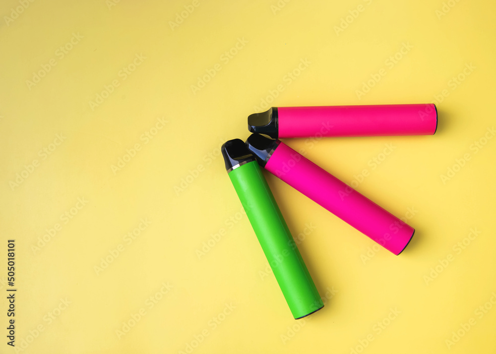 Three bright electronic cigarettes lie on a yellow background place under the inscription Three bright electronic cigarettes lie on a yellow background place under the inscription
