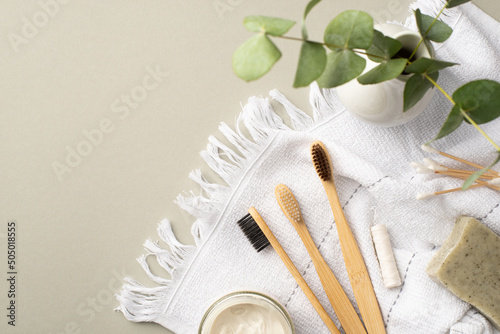 Eco friendly concept. Top view photo of bamboo toothbrushes toothpaste jar cotton buds dental floss soap white towel and vase with eucalyptus on isolated pastel grey background with empty space