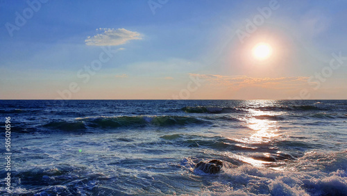 Colorful sunset with large sun under the sea waves.