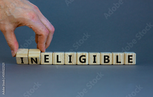Eligible or ineligible symbol. Businessman turns wooden cubes and changes words Ineligible to Eligible. Beautiful grey table grey background. Business eligible or ineligible concept. Copy space.